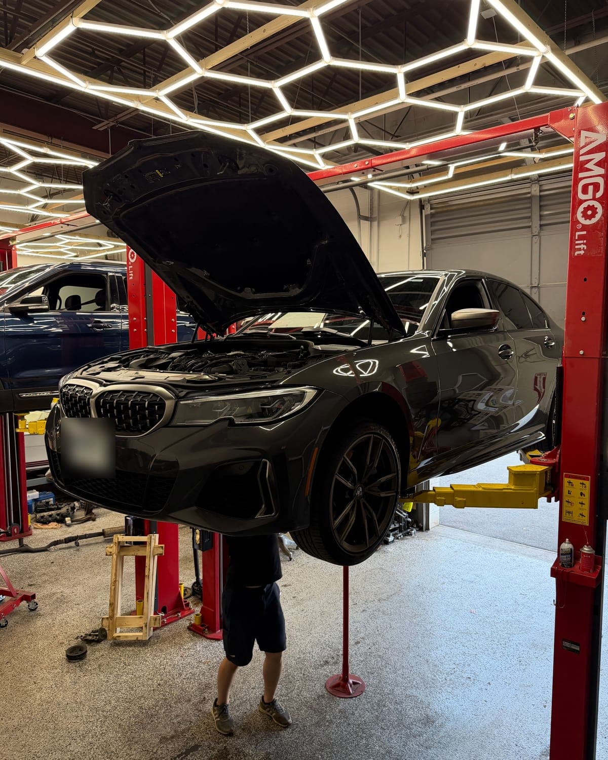 BMW repair in Manchester, NH: a gray BMW 3 Series raised on a lift with its hood open under the hexagon lights at Pro Tech Auto.