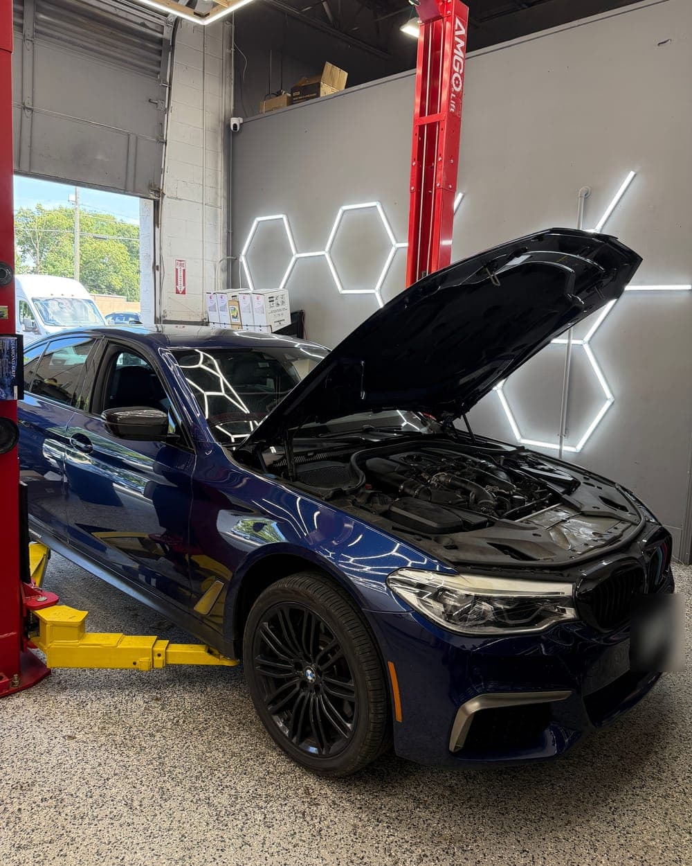 Blue BMW 5 Series with its hood open for scheduled maintenance in the Pro Tech Auto bay in Manchester, NH.