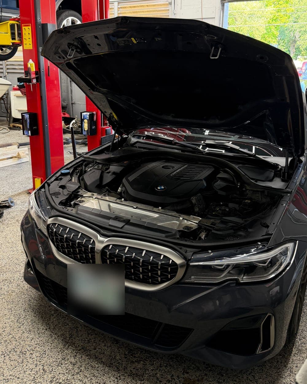 Engine bay of a gray BMW M340i with the hood open at Pro Tech Auto in Manchester, NH, showing its B58 turbocharged inline-six.