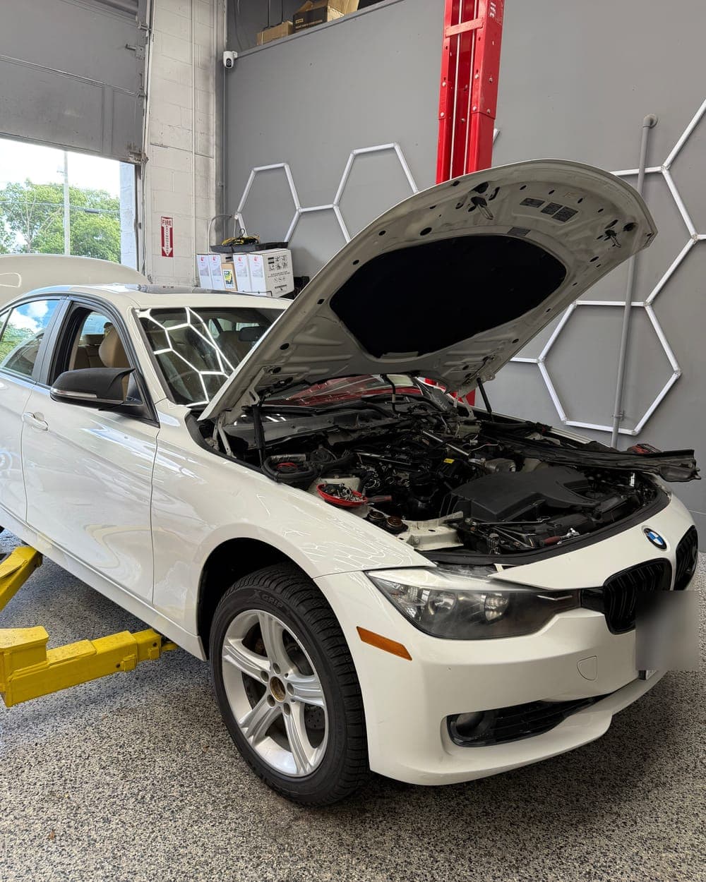 White BMW F30 3 Series with the hood up and engine work in progress in the Pro Tech Auto bay in Manchester, NH.