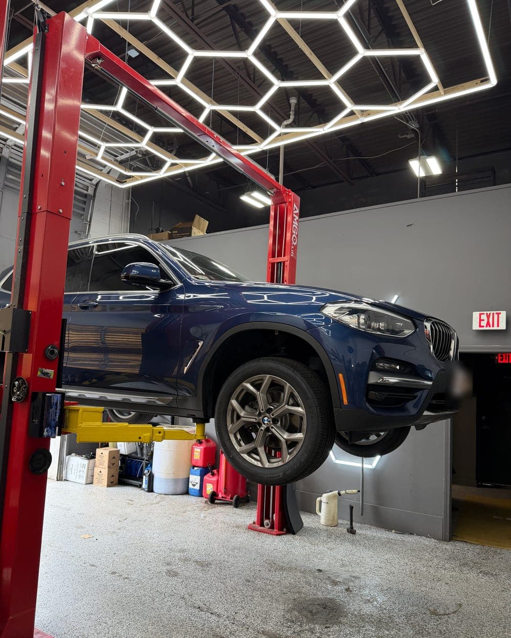 Blue BMW X3 raised on a lift under the hexagon lights at Pro Tech Auto in Manchester, NH.