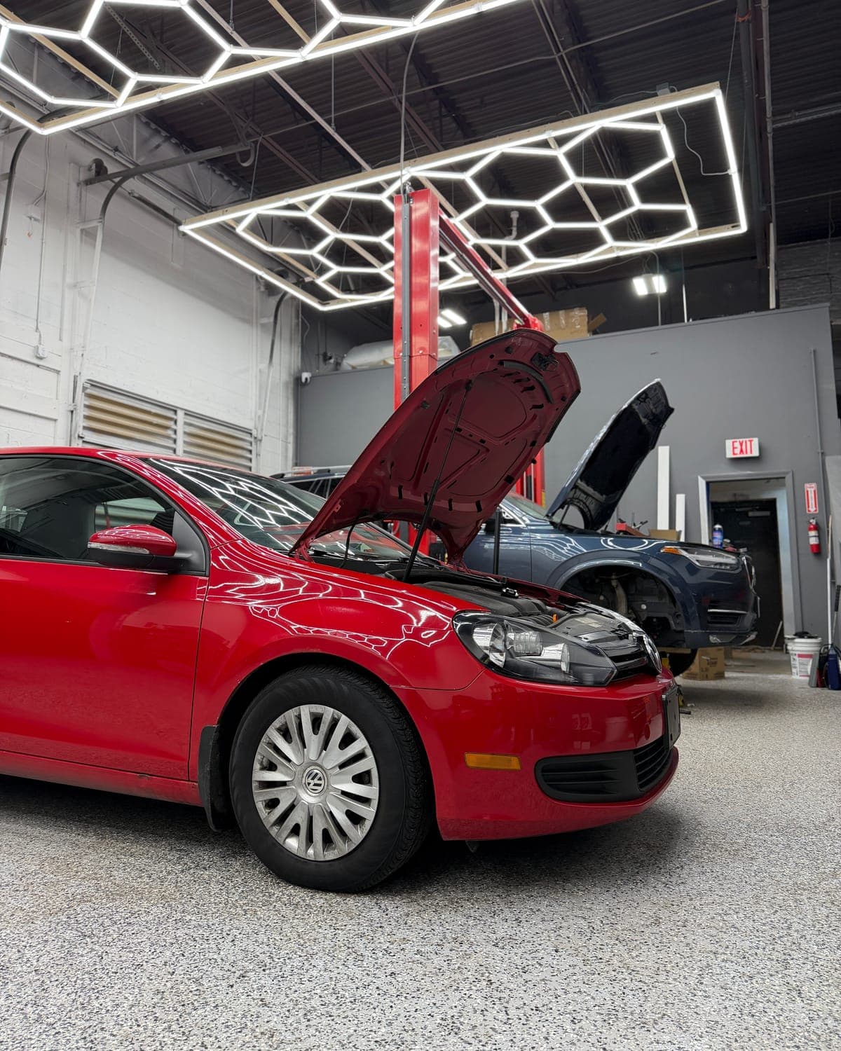Red Volkswagen Golf with its hood up in the Pro Tech Auto service bay in Manchester, NH.