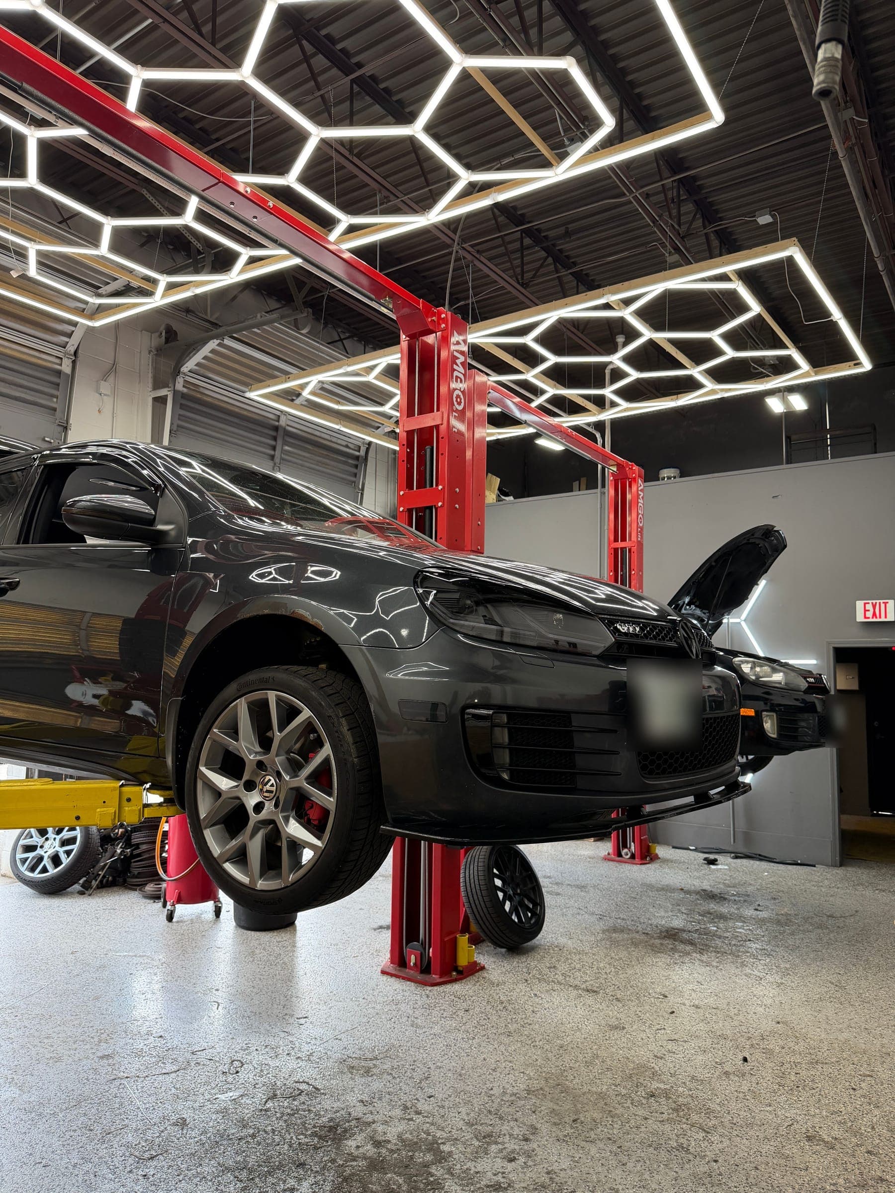Volkswagen repair in Manchester, NH: a gray Mk6 GTI raised on a lift at Pro Tech Auto, with a second GTI in the bay behind it.