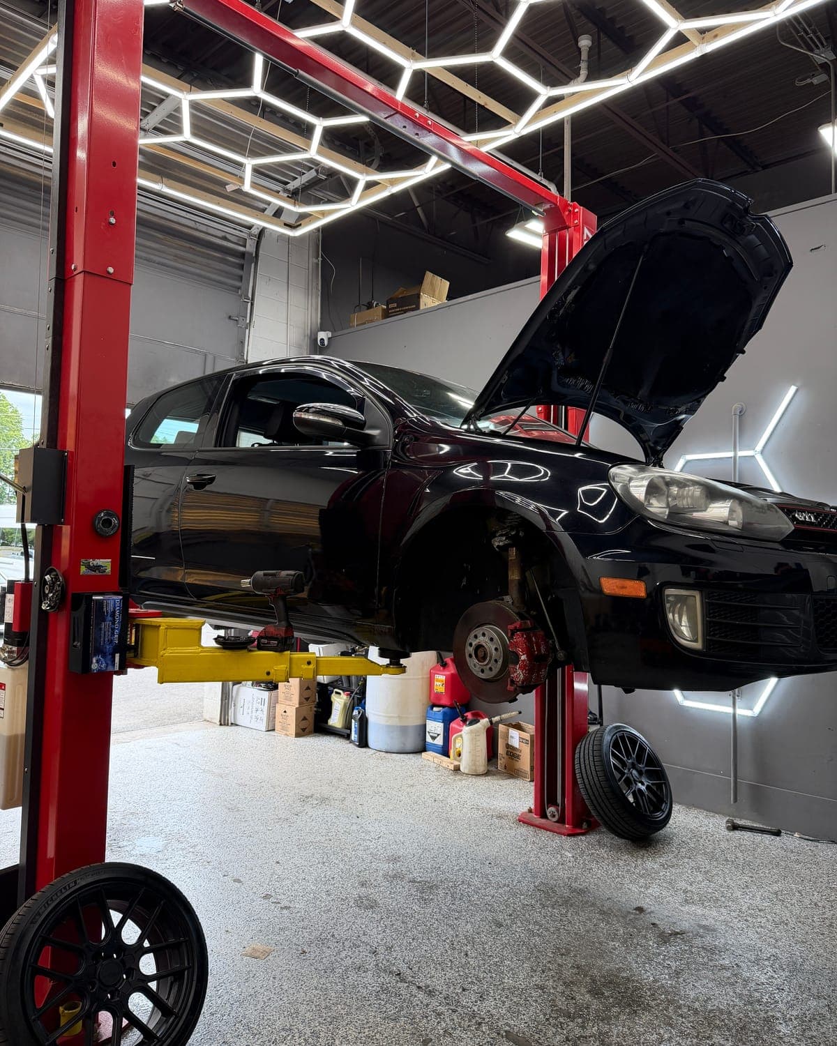 Black Volkswagen GTI on a lift at Pro Tech Auto in Manchester, NH, with the front wheel off and the brake rotor and caliper exposed.